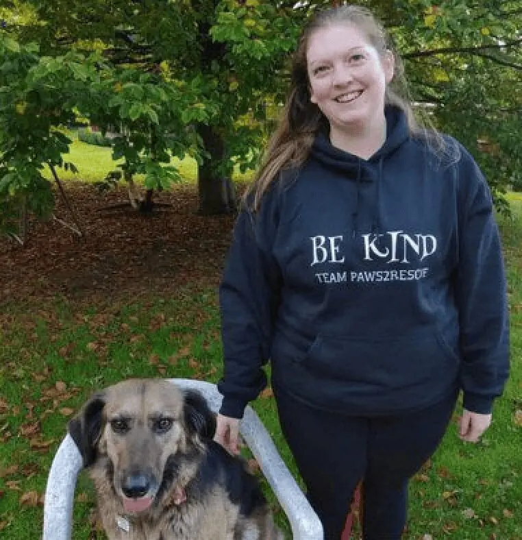 A photo of Paws2Rescue team member Danica stood outside next to a dog in a chair